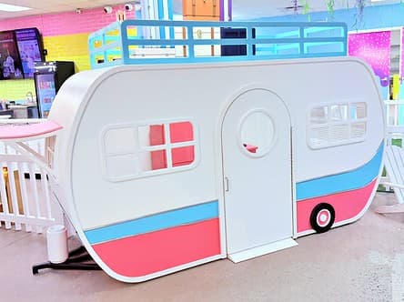 Jubilee's RV Camper, a white vintage-style trailer with pink and blue stripes and a railed roof deck