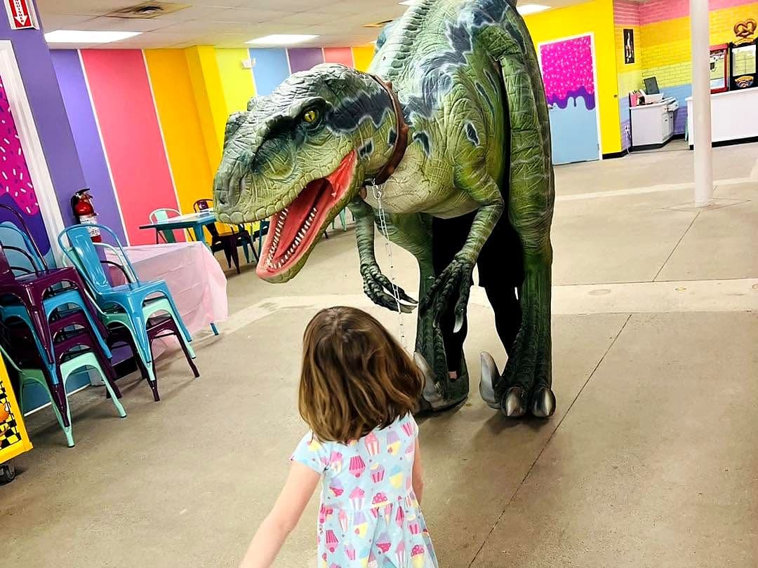 Little girl in a cupcake dress meeting a life-size dinosaur at the studio