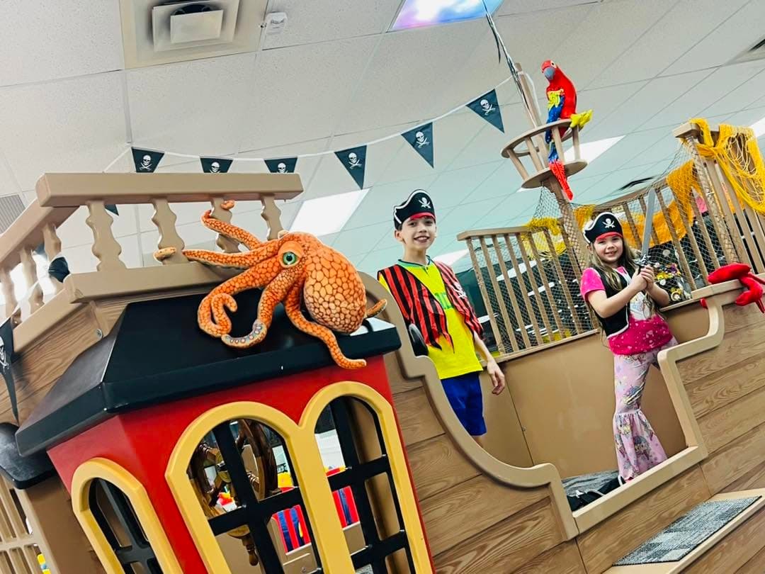 Boy and girl dressed as pirates waving a sword aboard the play pirate ship