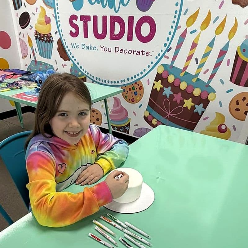 Smiling girl decorating a white fondant cake with food markers
