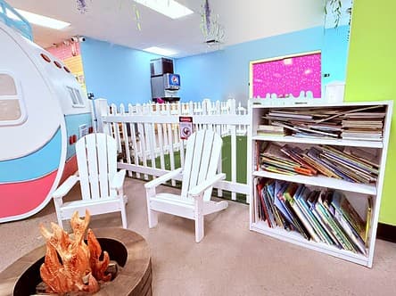 Reading nook with white Adirondack chairs around a pretend campfire and a shelf of picture books