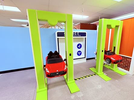 Two bright green car lifts holding red ride-on sports cars in the mechanic's garage