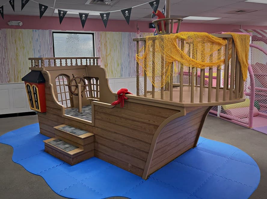 Easton's wooden Pirate Ship with a captain's wheel, steps and a rope net, on a blue water mat