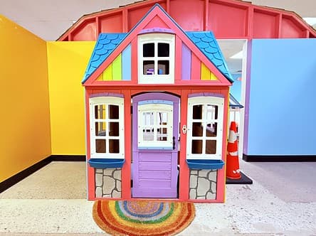 Rainbow Mini Mansion cottage with a blue roof, purple door and a rainbow rug at the step